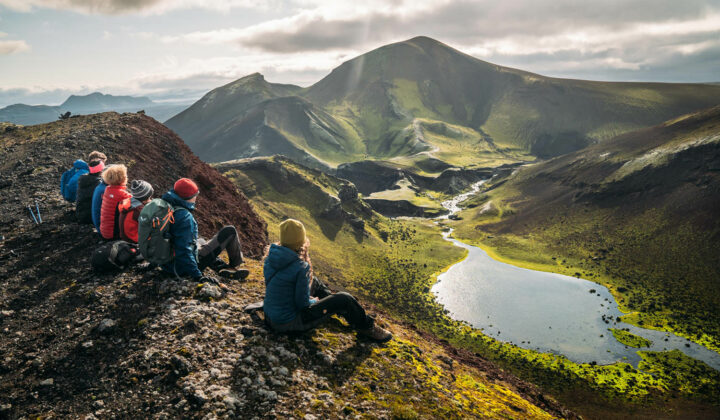 Hikers rest as they gaze upon a lake situated in the dramatic landscape of Iceland.