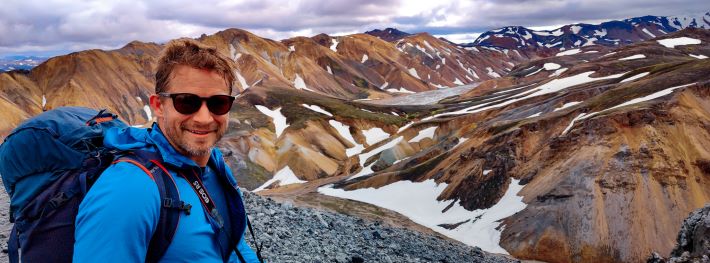 A hiker posing in front of a snow-glazed mountains and canyons of Laugavegur