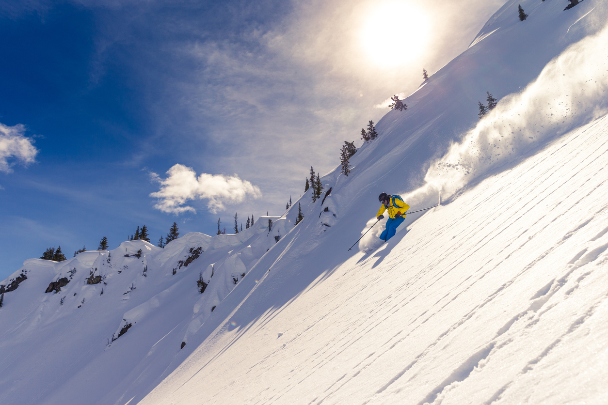A skier going down the hill by the trees.