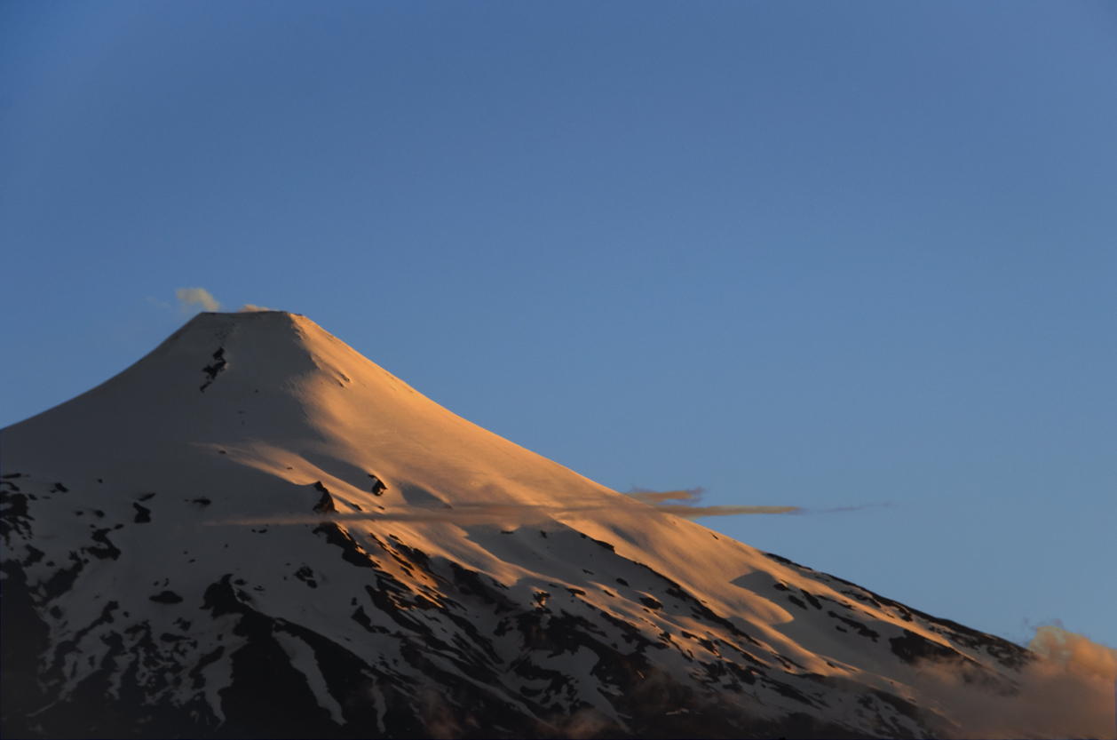 Close shot of the top of a volcano in Patagonia during sunset. The snowy cap is the hue of orange
