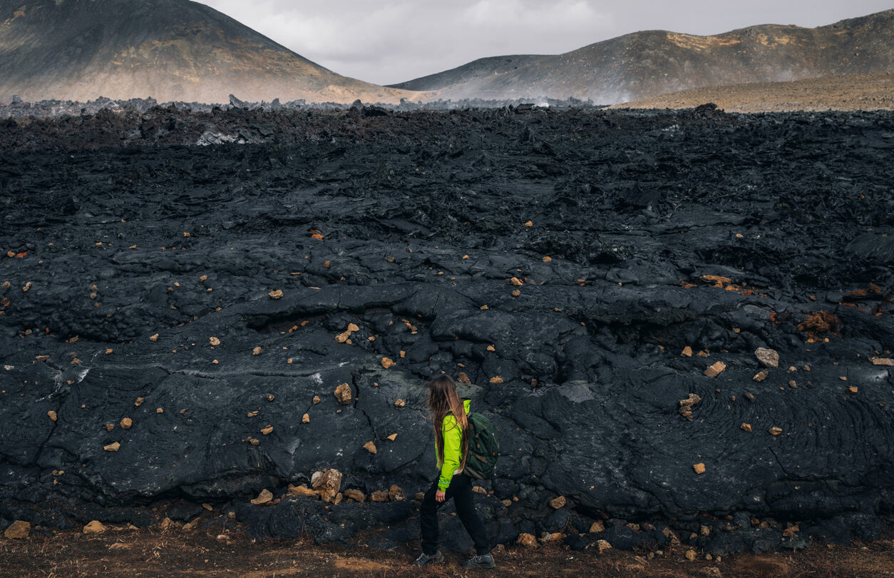 A woman hiking beside the firmed up lava close to the site of an erupting Iceland volcano.