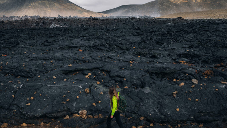 A woman hiking beside the firmed up lava close to the site of an erupting Iceland volcano.