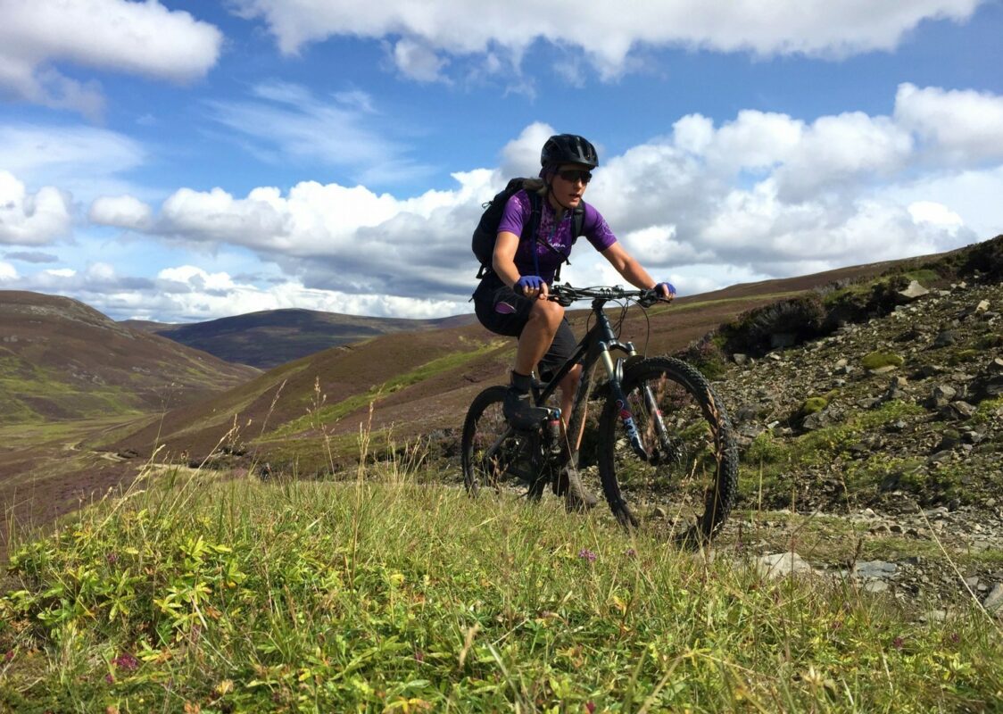 A mountain biker riding uphill along a trail in the Scottish Highlands.
