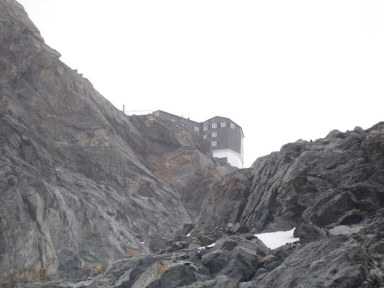 A high-altitude cabane, mountain hut, in the Swiss Alps, perched atop a massive rock formation.