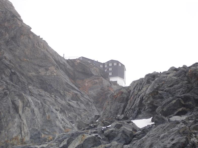 A high-altitude cabane, mountain hut, in the Swiss Alps, perched atop a massive rock formation.
